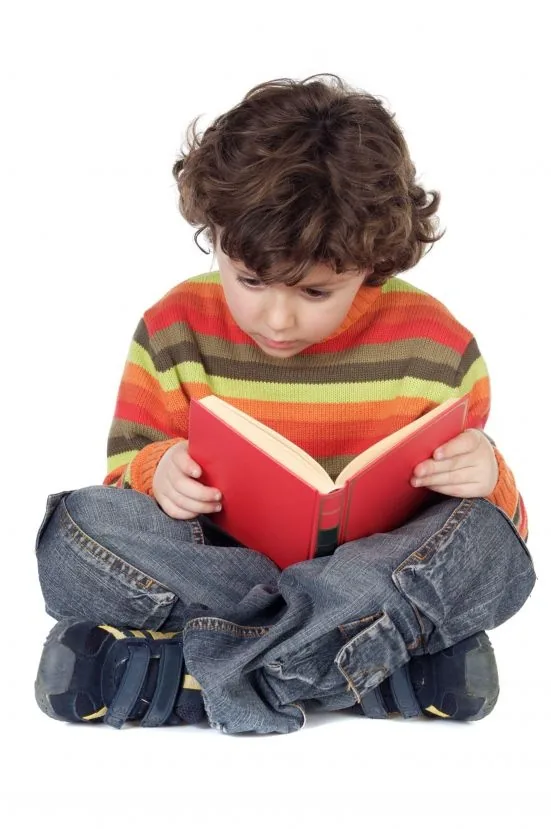 Young child in a colorful striped sweater reading a red book with full concentration